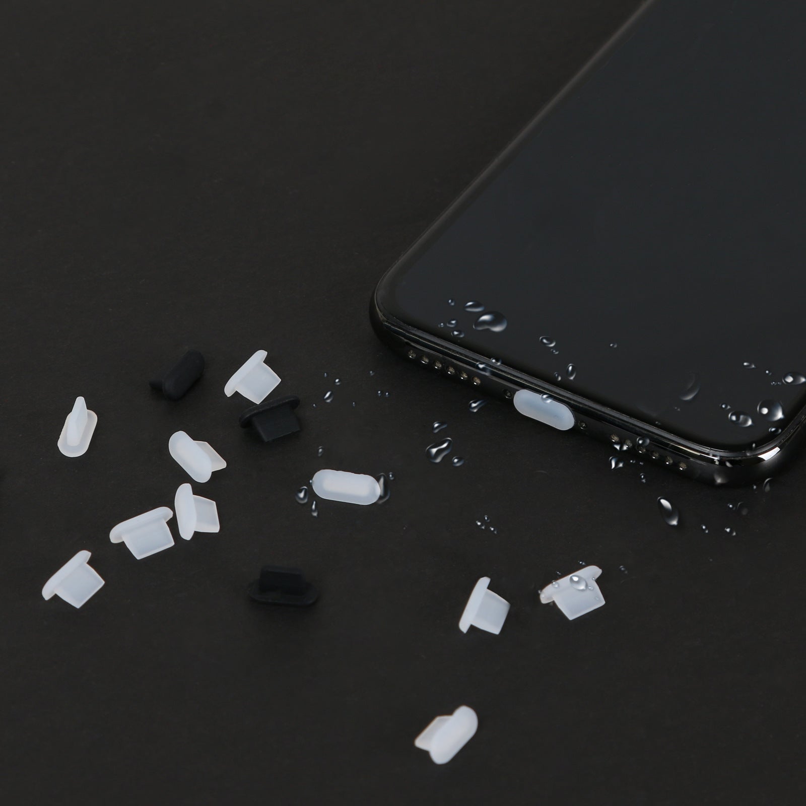 Klare silikone støvpropper liggende ved siden af en iPhone med vanddråber, viser vandafvisende effekt